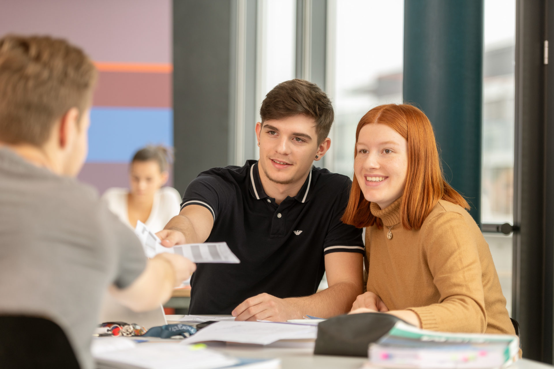 Lernende um ein Pult herum platziert, die untereinander Bläter austauschen.