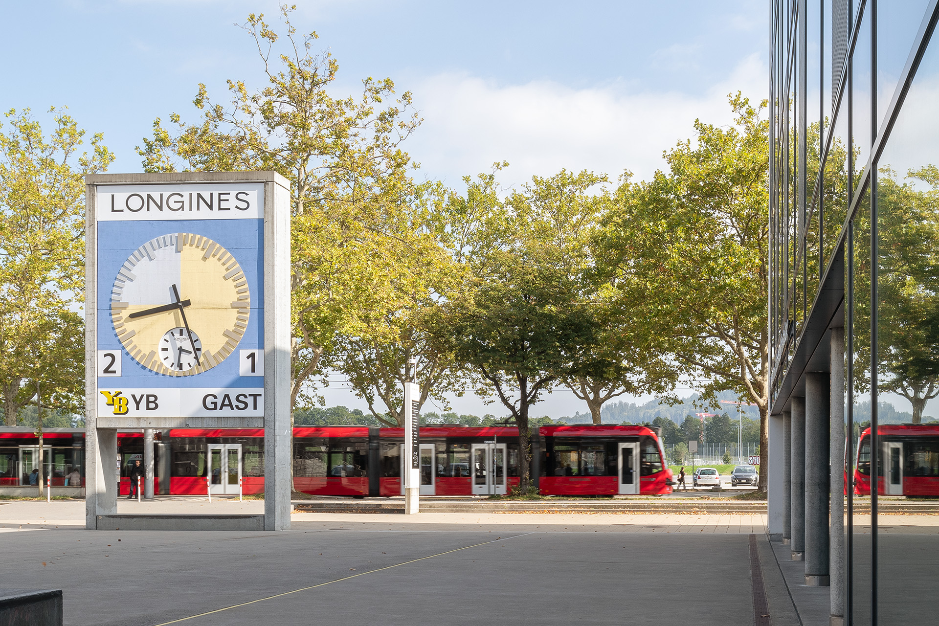 In der Mitte des Bildes ist die YB Uhr dahinter Bäume sowie das 9 Tram. Links ist die Gebäudefront vom bwd Gebäude.